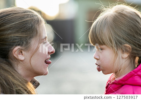 Close up portrait of young mom and her daughter girl making faces to each other outdoors. Close up portrait of young mom and her daughter girl making faces to each other outdoors. 127503917