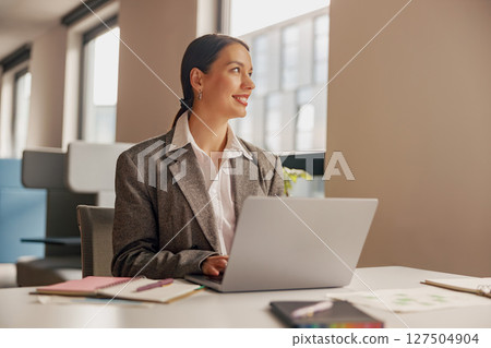A skilled professional woman works on a laptop in a modern, creative office environment 127504904