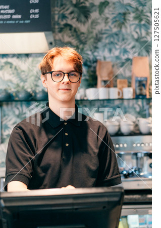 Young waiter serving customer at cash point in cafe. Man working with POS terminal. Cashier, barista checking for payment receipt. Hospitality, server and preparing a slip at the till in coffee shop. 127505621