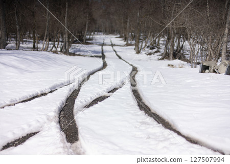A snowy road with a car trail A snowy road with a car trail 127507994