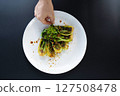 A hand adds garnishing to freshly prepared bok choy on a white plate in a vibrant kitchen setting. 127508478