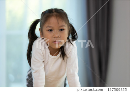 A young girl with pigtails is focused on her playtime activity. She appears deep in thought, surrounded by soft natural light filtering through windows in a comfortable setting. 127509855