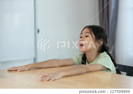 Young Girl Expressing Herself While Sitting at a Table in a Bright and Simple Indoor Setting During the Daytime 127509909