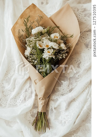 Bouquet of fresh flowers wrapped in brown paper on a cream lace background 127510395