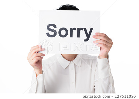A person wearing a white shirt holding a piece of paper with the word "Sorry" written on it 127511050
