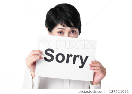 A middle-aged woman looking up and holding a piece of paper that says "Sorry" 127511051