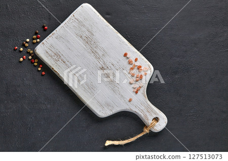 white wooden cutting board and scattered pink salt and peppercorns on black concrete table 127513073
