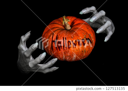 Bony pale monsters hands with sharp nails and pumpkin with lettering Halloween between them, isolated on black. Bony pale monsters hands with sharp nails and pumpkin with lettering Halloween between them, isolated on black. 127513135
