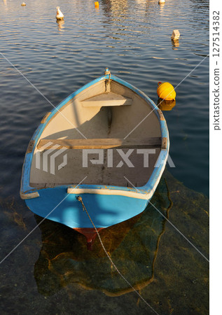 Old Dinghy Floating in Calm Harbor Waters at Sunset 127514382