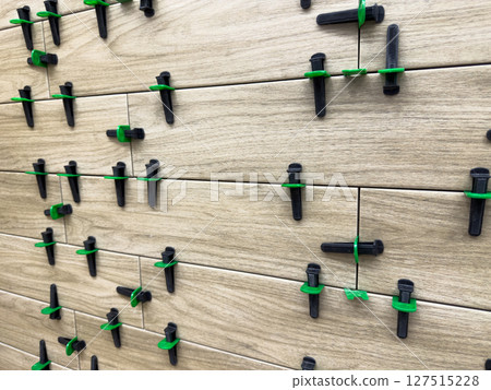 Close up view of ceramic tile installation using plastic leveling spacers and clips for precise. Alignment on wooden textured tile during floor renovation or interior construction process Close up view of ceramic tile installation using plastic leveling spacers and clips for precise. Alignment on wooden textured tile during floor renovation or interior construction process 127515228