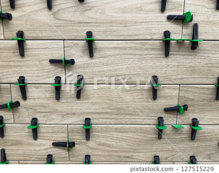 Tile installation in progress showing close up of wood look ceramic tiles with green and black leveling spacers. Ensuring precise alignment and even spacing during flooring renovation work 127515229