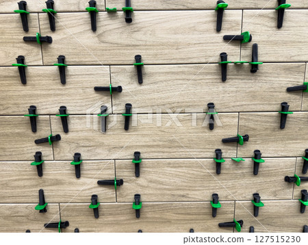 Ceramic tiles being installed with leveling system. Black and green spacers keep the surface even and joints straight, showing the precise alignment in construction or renovation work Ceramic tiles being installed with leveling system. Black and green spacers keep the surface even and joints straight, showing the precise alignment in construction or renovation work 127515230