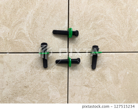 Close up of beige ceramic tiles aligned with tile leveling system. Precision tools create straight grout lines and a smooth, professional finish during modern interior installation work 127515234