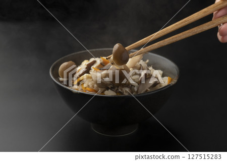 Using chopsticks to lift up rice cooked in a clay pot with mushrooms in a rice bowl 127515283