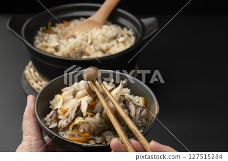 Using chopsticks to lift up rice cooked in a clay pot with mushrooms in a rice bowl 127515284