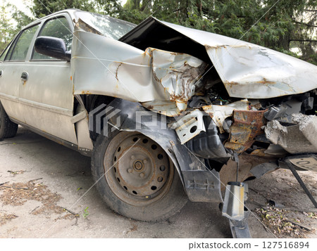 Close up view of heavily damaged car after traffic accident, with crumpled front fender, rust, and exposed engine parts on an urban roadside 127516894