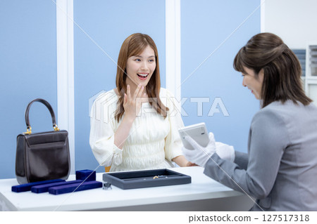 一位女士正在接受買家對她的包包和貴金屬的評估 127517318