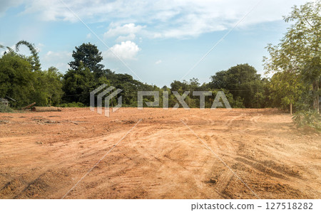 Empty dry cracked swamp reclamation soil, land plot for housing construction project with car tire print in rural area and beautiful blue sky. 127518282