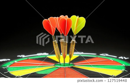 Darts with heart-shaped tips on a colorful dartboard taken in a well-lit indoor setting 127519448