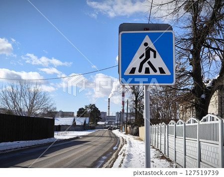 Pedestrian crossing road sign against the background of snow-covered street. blue pedestrian crossing sign on winter street 127519739