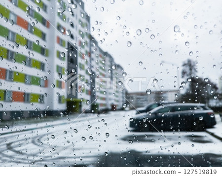 water drops on glass surface, view through car window with rain drops, winter cityscape through the car window, multi-storey house and parking for cars, rainy weather. 127519819