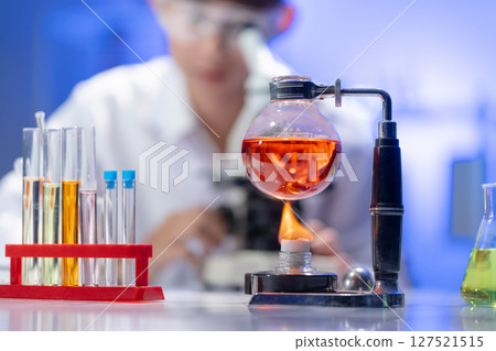 Scientific experiment heating a red chemical liquid in a Florence flask over an alcohol burner in a research lab. 127521515