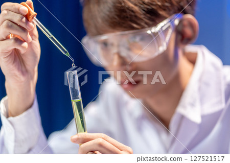 A focused young Asian scientist conducting a chemical experiment in the laboratory. 127521517