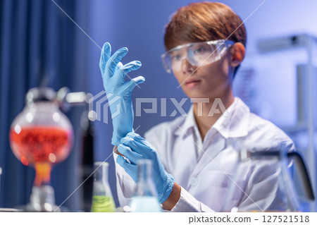 A young Asian male scientist putting on blue rubber gloves  in the laboratory. 127521518
