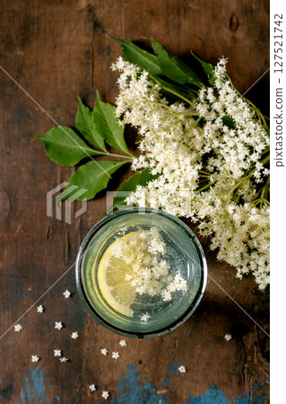 Glass elderflower beverage with lemon slice fresh white elderflower blossoms on rustic wooden background. Natural herbal drink concept. 127521742