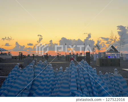 Colorful Blue and White Striped Umbrellas Stacked at a Sea Beach, Sunset Background 127522016