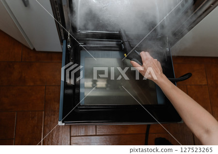 High-angle view of cleaning company worker washing gas oven with steam cleaner in kitchen, holding steam cleaner gun removing grease and ensuring hygienic cooking environment, close-up cropped shot High-angle view of cleaning company worker washing gas oven with steam cleaner in kitchen, holding steam cleaner gun removing grease and ensuring hygienic cooking environment, close-up cropped shot 127523265