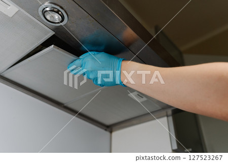 Low-angle view of man wearing blue gloves removing kitchen hood filter for cleaning with steam cleaner, ensuring thorough maintenance and hygiene in kitchen room. Concept of cleanliness and household. 127523267