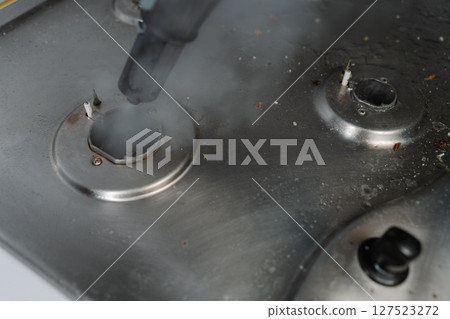 Close-up steam cleaning gas stove surface, eliminating burned food and grease, restoring kitchen surface to pristine condition with sanitizing process. Concept of modern housekeeping appliance. Close-up steam cleaning gas stove surface, eliminating burned food and grease, restoring kitchen surface to pristine condition with sanitizing process. Concept of modern housekeeping appliance. 127523272