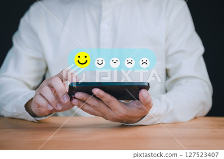 Person holding a smartphone select a happy face icon from a feedback scale with five emoji options, symbolizing customer satisfaction, review, and positive user experience in an online feedback 127523407