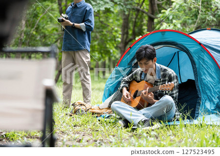 Family bonding outdoors. Young man playing guitar while father captures moments with camera. Family bonding outdoors. Young man playing guitar while father captures moments with camera. 127523495