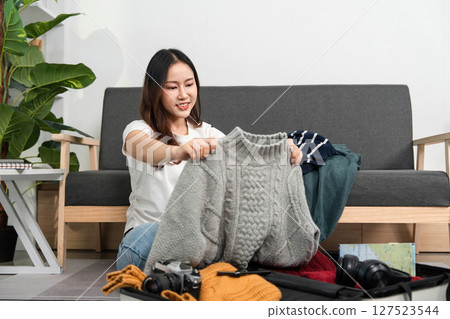 Organizing Clothes for Travel. A woman folds a sweater while packing her suitcase. 127523544