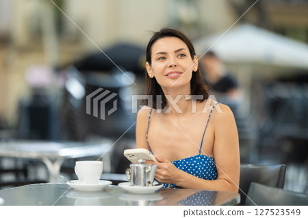 Brunette texting on smartphone screen during breakfast on cafe terrace. Drinking tea Brunette texting on smartphone screen during breakfast on cafe terrace. Drinking tea 127523549