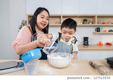 Family Cooking Fun. A mother pouring water while her son adds flour to a bowl. Family Cooking Fun. A mother pouring water while her son adds flour to a bowl. 127523550
