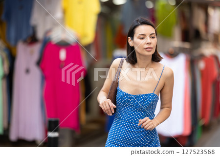 Young girl in blue dress is looking for something at street market - looking at goods with interest 127523568