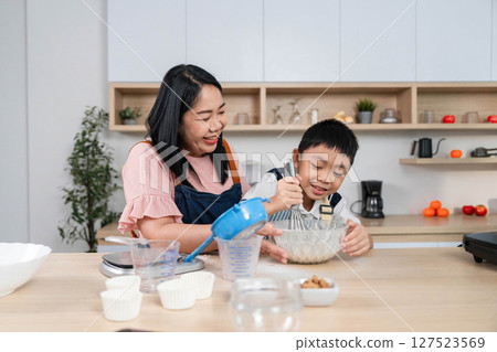 Family Cooking Together. A cheerful mother assists her son while they mix ingredients in the kitchen. 127523569