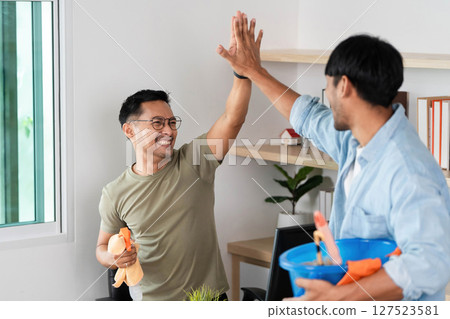 Teamwork in Cleaning. Two men celebrating after successfully organizing their workspace. 127523581