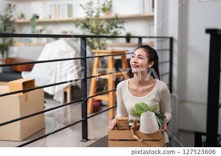 Moving and Home Organization. A young woman carrying plants and decor while relocating to a new space. Moving and Home Organization. A young woman carrying plants and decor while relocating to a new space. 127523606