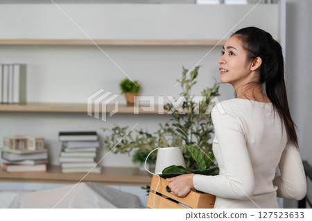 Moving and Unpacking. Woman smiling while carrying a crate with plants indoors. Moving and Unpacking. Woman smiling while carrying a crate with plants indoors. 127523633