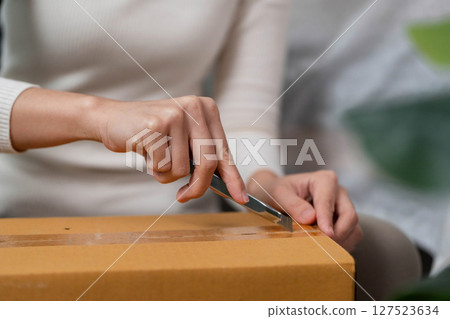 Moving process. Close-up of a woman opening a box with a utility knife. 127523634