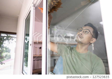 Window Cleaning and Maintenance. A man carefully cleaning a window in a bright living area. Window Cleaning and Maintenance. A man carefully cleaning a window in a bright living area. 127523635