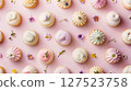 Beautiful flat lay of pastel frosted cupcakes and small flowers arranged on a soft pink background in an artistic pattern.  127523758
