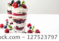 Two glasses of layered berry parfaits topped with whipped cream and fresh berries on a white surface, bright and appetizing.  127523797
