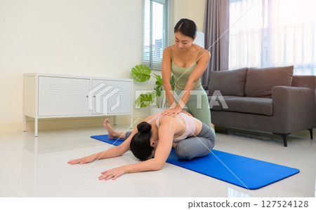 Two sporty girls practice yoga with partner at home. Trainer helps student to do seated forward fold exercise 127524128