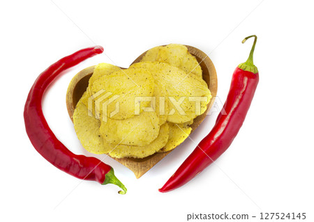 Chips with red pepper on a wooden plate are photographed from above. 127524145