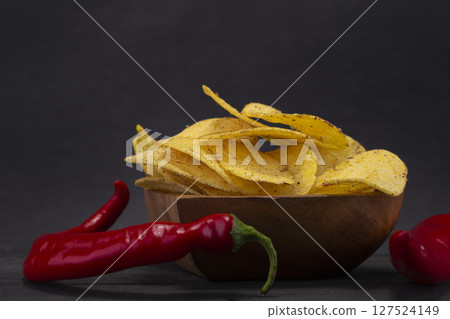 Chips with red pepper on a wooden plate on a gray background. 127524149